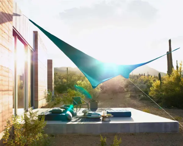 Terraza moderna con toldos vegetales que protegen del sol del desierto. Muebles cómodos y cactus al fondo.