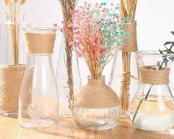 Botellas de cristal decoradas con cuerda, con flores secas y una rama de eucalipto.
