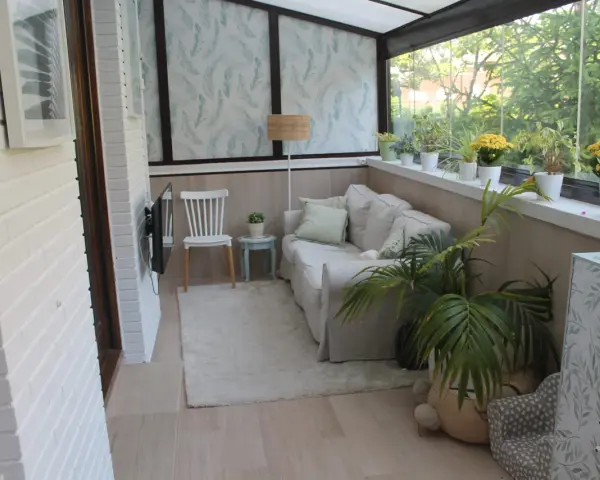 Acogedor salón en terrazas cerradas con encanto, con sofá, silla, plantas y vistas al exterior.