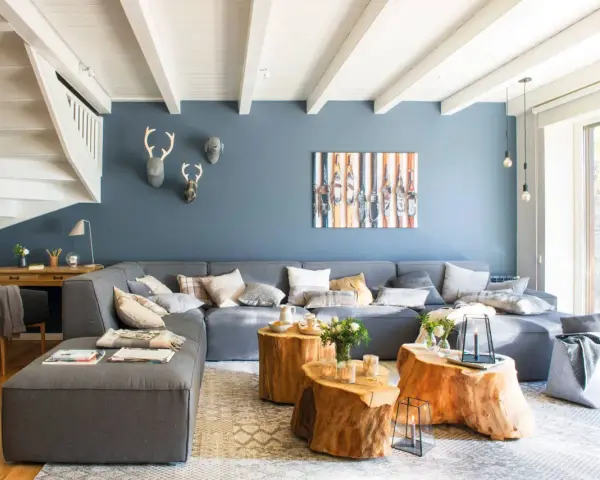 Sofá modular gris y pared azul crean un ambiente acogedor. Mesas de tronco y detalles en madera aportan calidez.