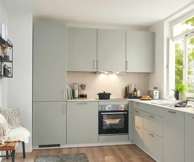 Moderna cocina de obra con armarios grises, electrodomésticos integrados y una ventana luminosa. Perfecta para crear tus platos favoritos.