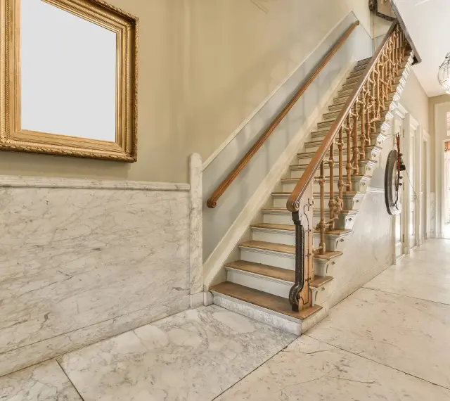 Elegante escalera con barandilla de madera y mármol para decorar rellano escalera comunidad. Un cuadro dorado adorna la pared.