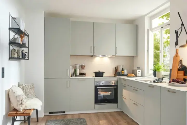 Moderna cocina de obra con armarios grises, electrodomésticos integrados y una ventana luminosa. Perfecta para crear tus platos favoritos.
