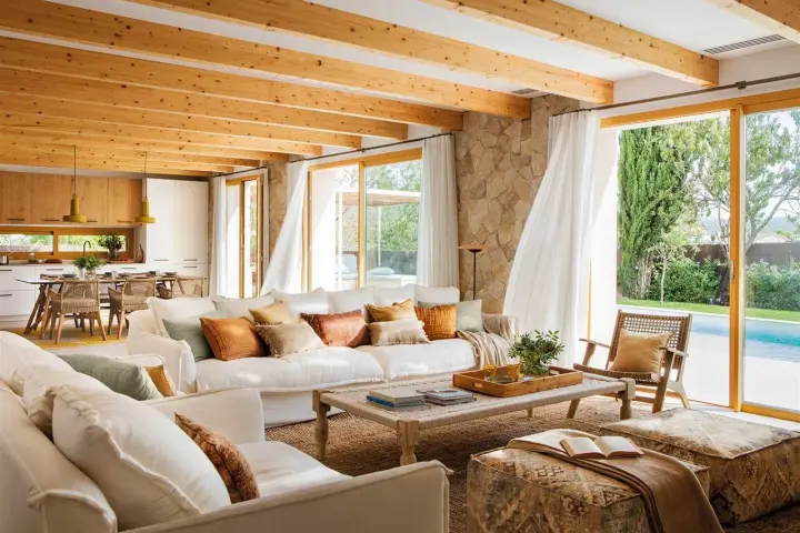 Salones blancos y madera con vigas expuestas, sofás cómodos y vistas a una piscina.