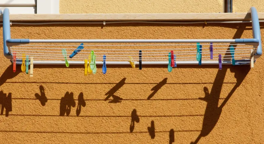 Tendedero exterior con pinzas de colores. Ideas para secar la ropa al sol, creando sombras divertidas en la pared.