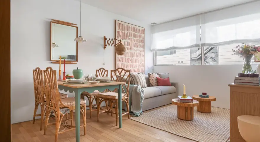 Ideas para decorar un piso pequeño con poco dinero: mesa de comedor de ratán, sofá acogedor y arte de pared llamativo.