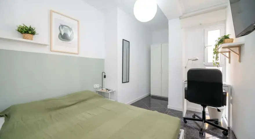 Habitación luminosa con cama, escritorio y armario. Ideal como piso para estudiantes, con decoración moderna y plantas.