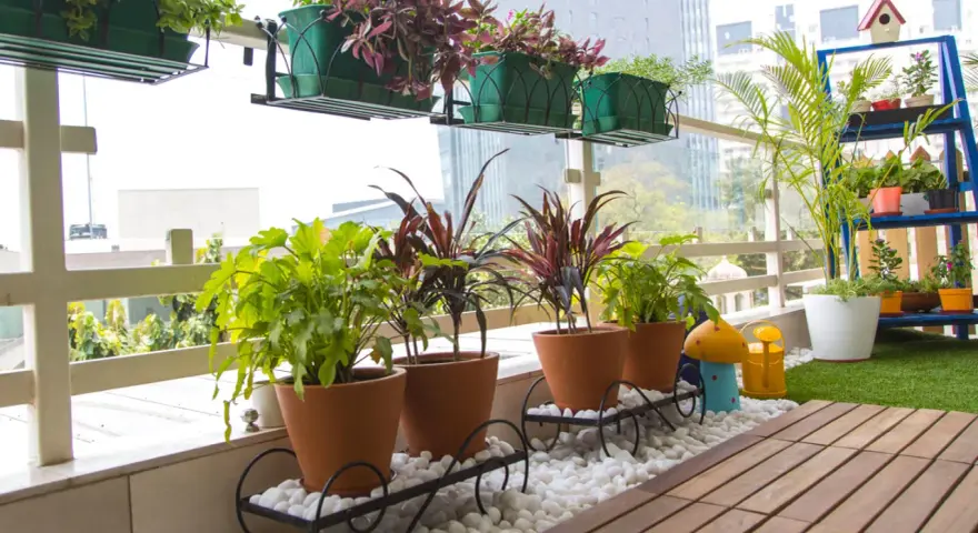 Balcón lleno de plantas en macetas, ideal para decorar terrazas barato. Césped artificial y suelo de madera completan el espacio.