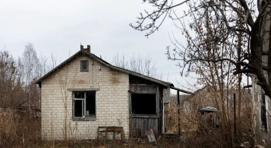 Casa de ladrillo blanco, abandonada, con ventanas rotas y vegetación seca. Un ejemplo de la ley sobre casas abandonadas.