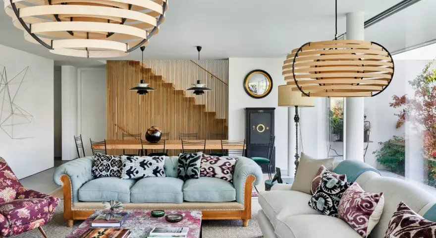 Elegante salón con sofás claros, mesa de centro con libros y lámparas de madera. El minimalismo en casa se refleja en la escalera de madera y la decoración cuidada.