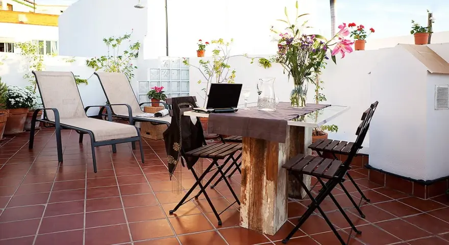 Terraza con tumbonas, mesa y sillas, ideal para uso privativo. Flores y plantas decoran el espacio.
