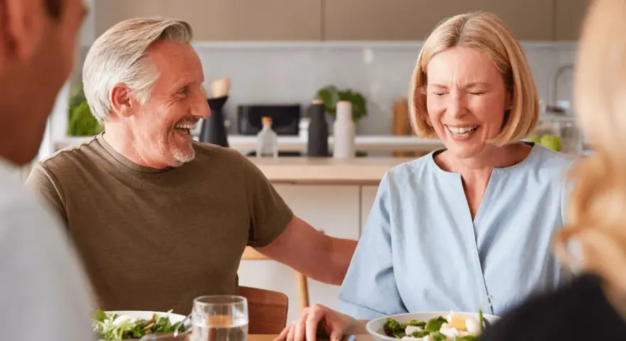 Padre e hijo ríen mientras planean comprar vivienda a medias. Comida familiar en la cocina.