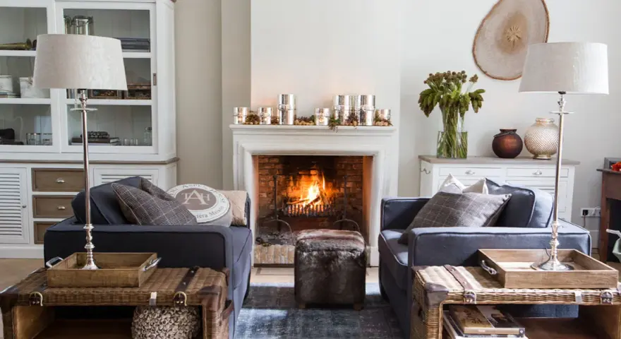Ideas para decorar la repisa de una chimenea: velas, piñas y un jarrón con ramas secas crean un ambiente acogedor.