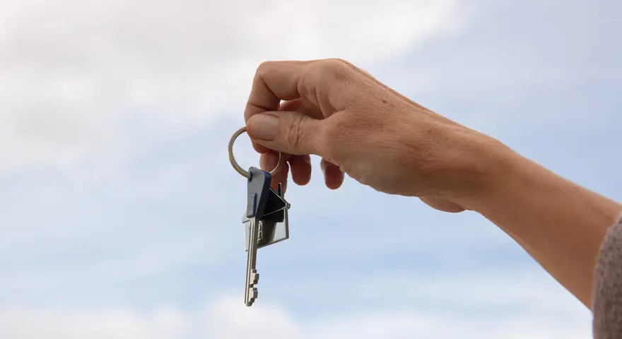 Mano sostiene un llavero con dos llaves y un dije de casa. La custodia llaves comunidad representa el acceso a un hogar compartido.