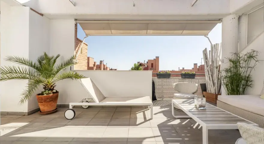Encantadora decoracion terrazas aticos: tumbona, mesa de centro, sillón y plantas crean un oasis urbano.