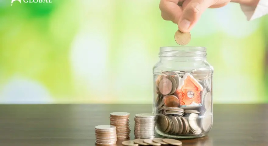 Mano deposita moneda en alcancía con casa, pensando qué pasa si no pago el último mes de alquiler.
