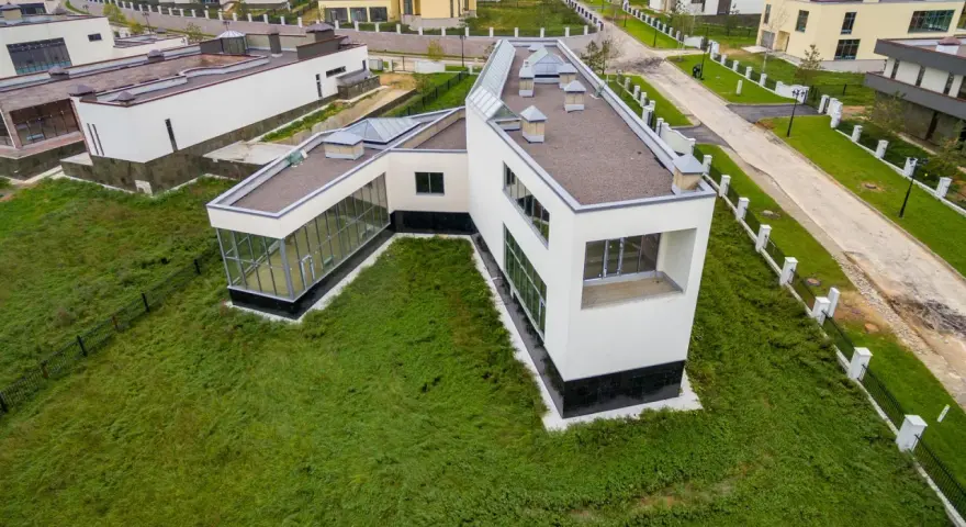 Casa moderna con grandes ventanales y tejado plano, rodeada de césped. Se puede poner una casa prefabricada en un terreno urbano como esta.