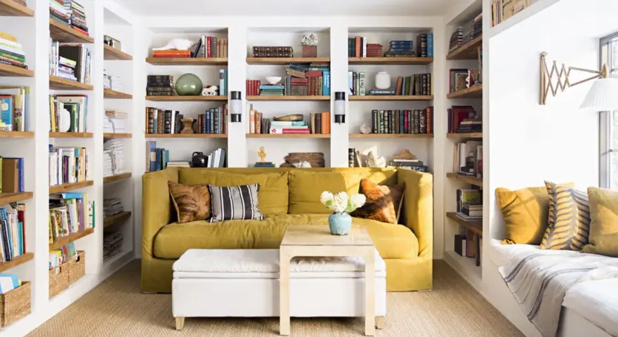 Sofá amarillo y estanterías llenas de libros, como si fueran casas que no necesitan permiso de obra. Un espacio acogedor para leer.