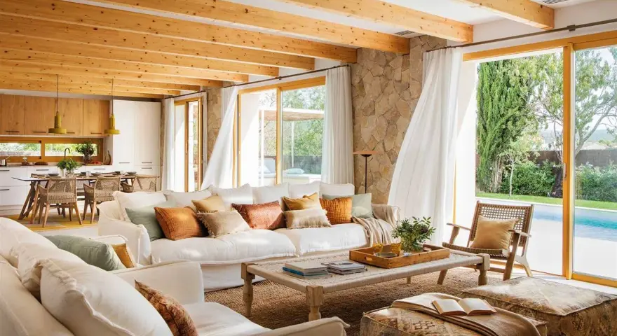 Salones blancos y madera con vigas expuestas, sofás cómodos y vistas a una piscina.
