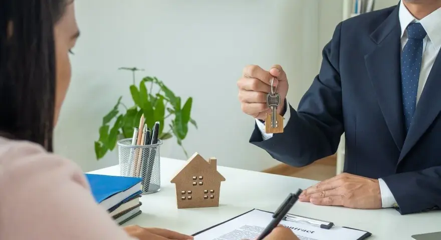 Agente inmobiliario entrega llaves a cliente. Un modelo de casa y un contrato sobre la mesa, ideal para referencia precios alquiler.