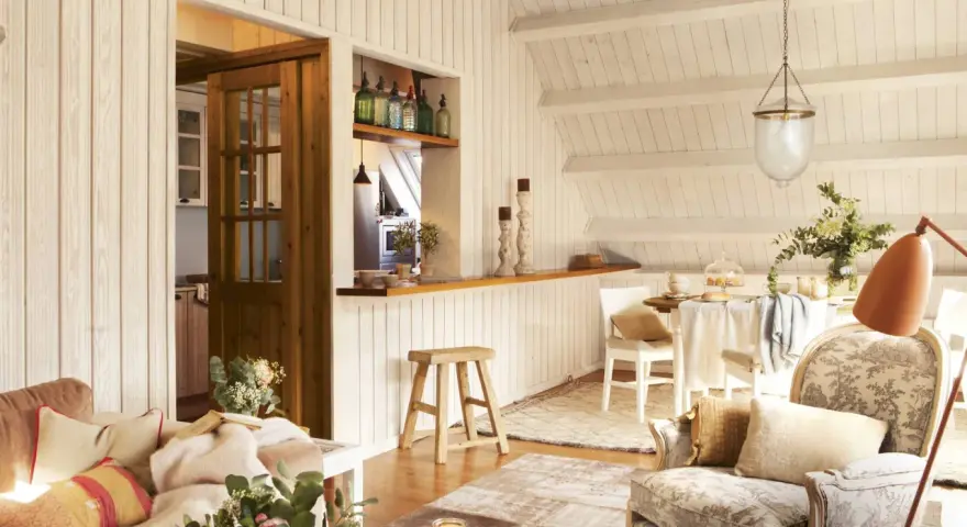 Acogedora buhardilla con encanto, con sofá, sillón estampado, mesa de comedor y cocina abierta.