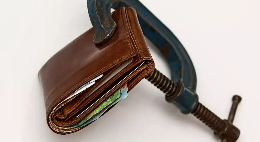 Cartera de cuero apretada en una prensa. El heredero no paga gastos de vivienda, el dinero está bajo presión.