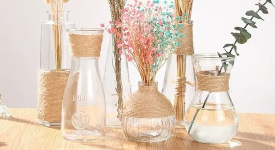 Botellas de cristal decoradas con cuerda, con flores secas y una rama de eucalipto.