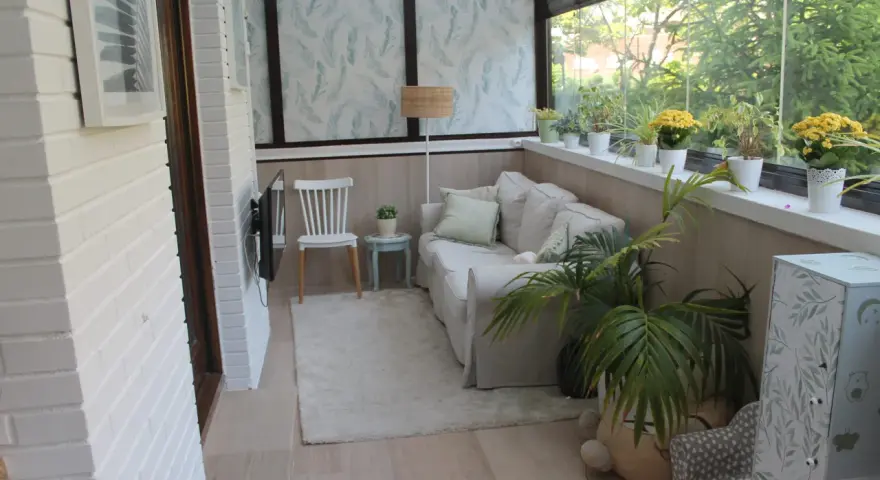 Acogedor salón en terrazas cerradas con encanto, con sofá, silla, plantas y vistas al exterior.