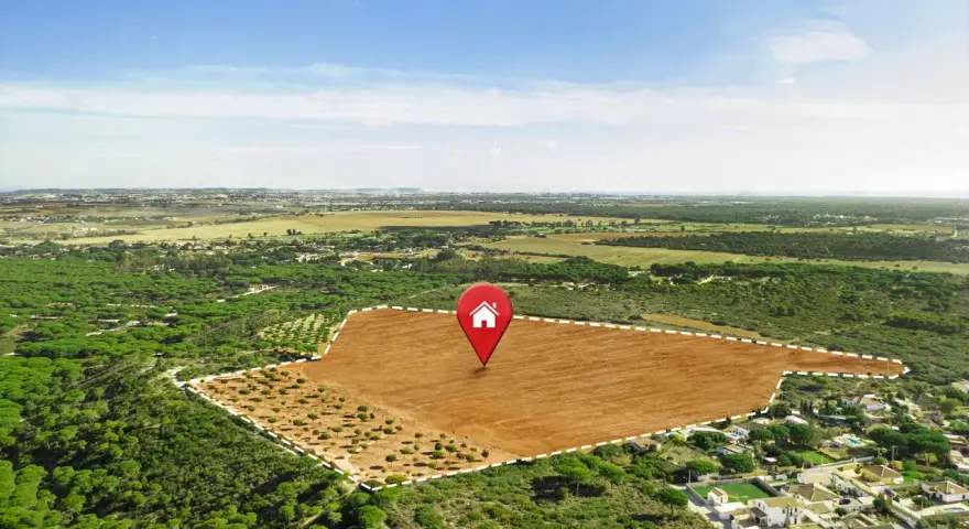 Vista aérea de varios tipos de terrenos: un campo marrón arado, un bosque de pinos y un área residencial.
