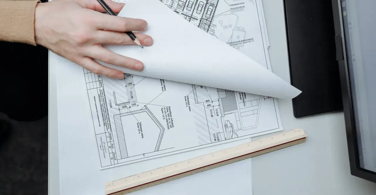 Manos revisando planos de construcci&oacute;n. Se puede escriturar sin c&eacute;dula de habitabilidad, seg&uacute;n los detalles en el documento.