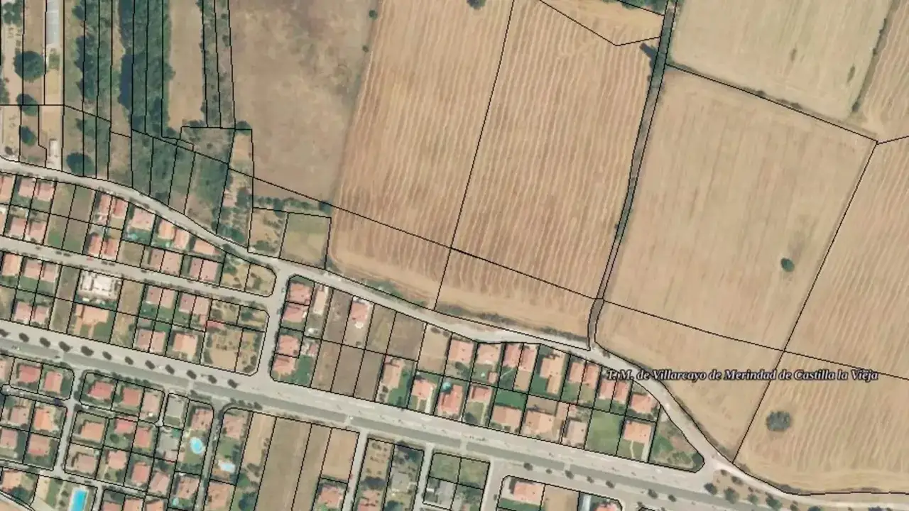 Vista a&eacute;rea de parcelas urbanizadas con casas y un gran terreno r&uacute;stico adyacente, con campos de cultivo y vegetaci&oacute;n.
