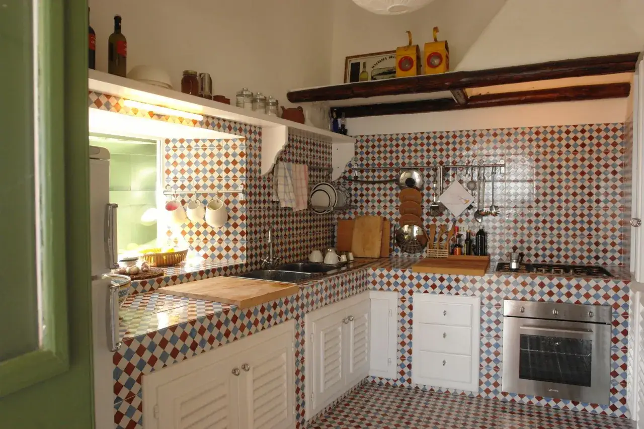 Encantadora cocina de obra con azulejos de rombos en tonos tierra y azul. Utensilios de cocina colgados y encimeras de madera.