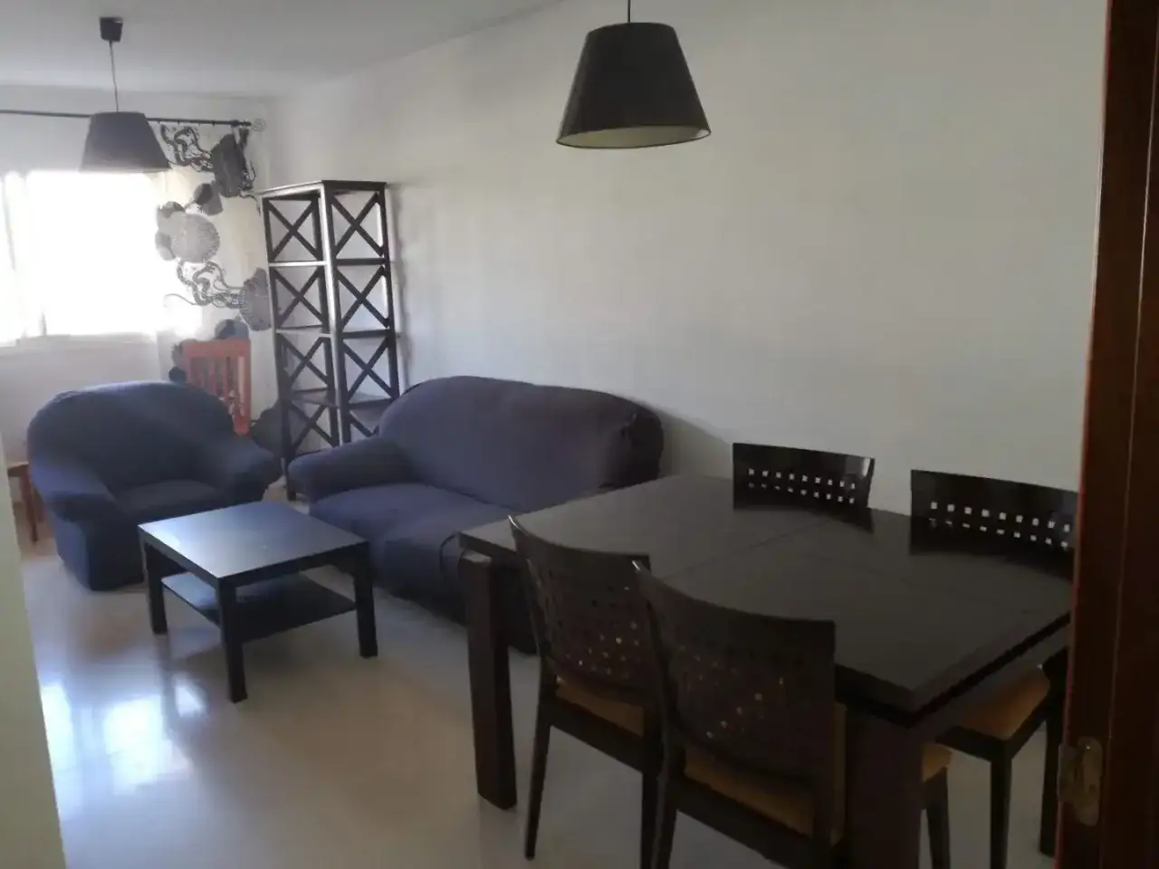 Sal&oacute;n de un piso para estudiantes con sof&aacute;, sill&oacute;n, mesa de centro y mesa de comedor con sillas.
