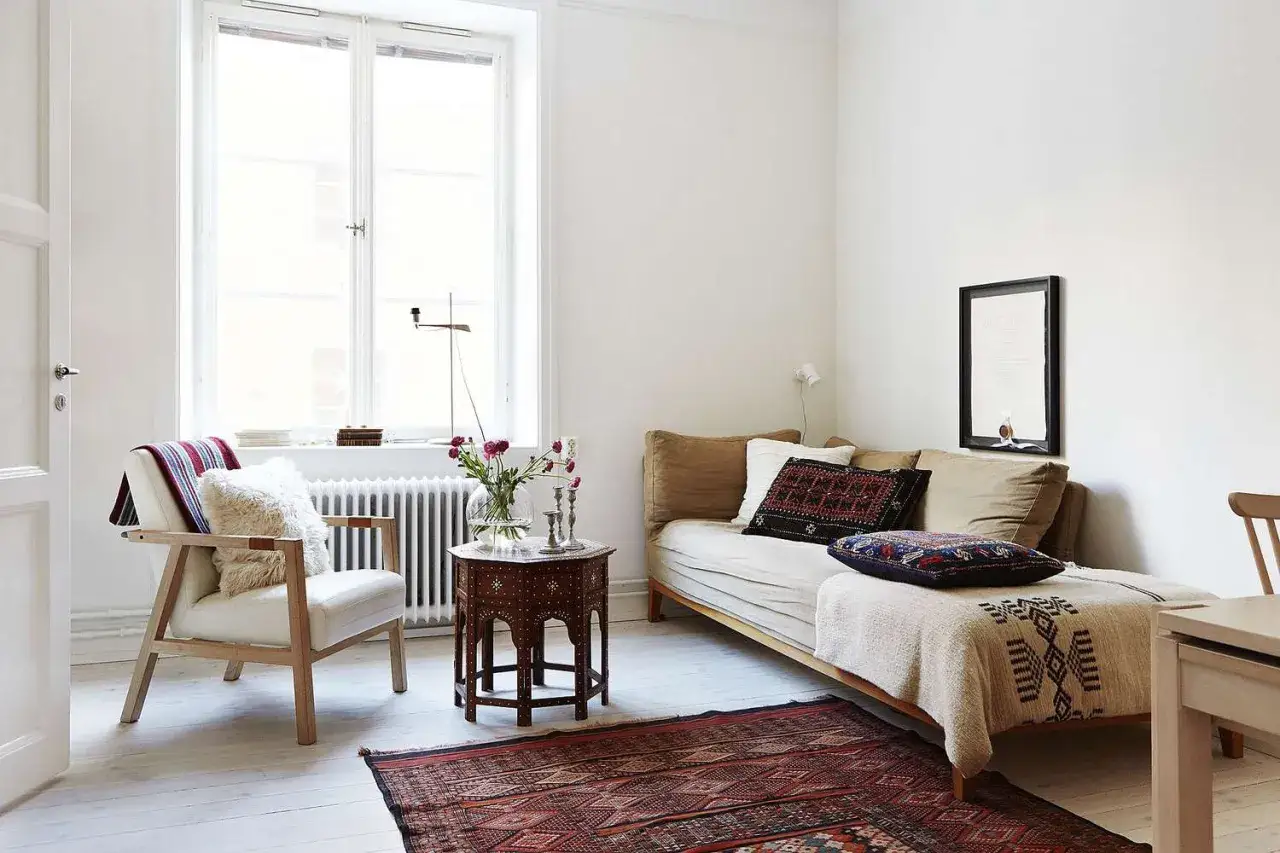 Ideas para decorar un piso peque&ntilde;o con poco dinero: sill&oacute;n blanco, sof&aacute; cama, mesa auxiliar marroqu&iacute;, alfombra oriental y cojines &eacute;tnicos.