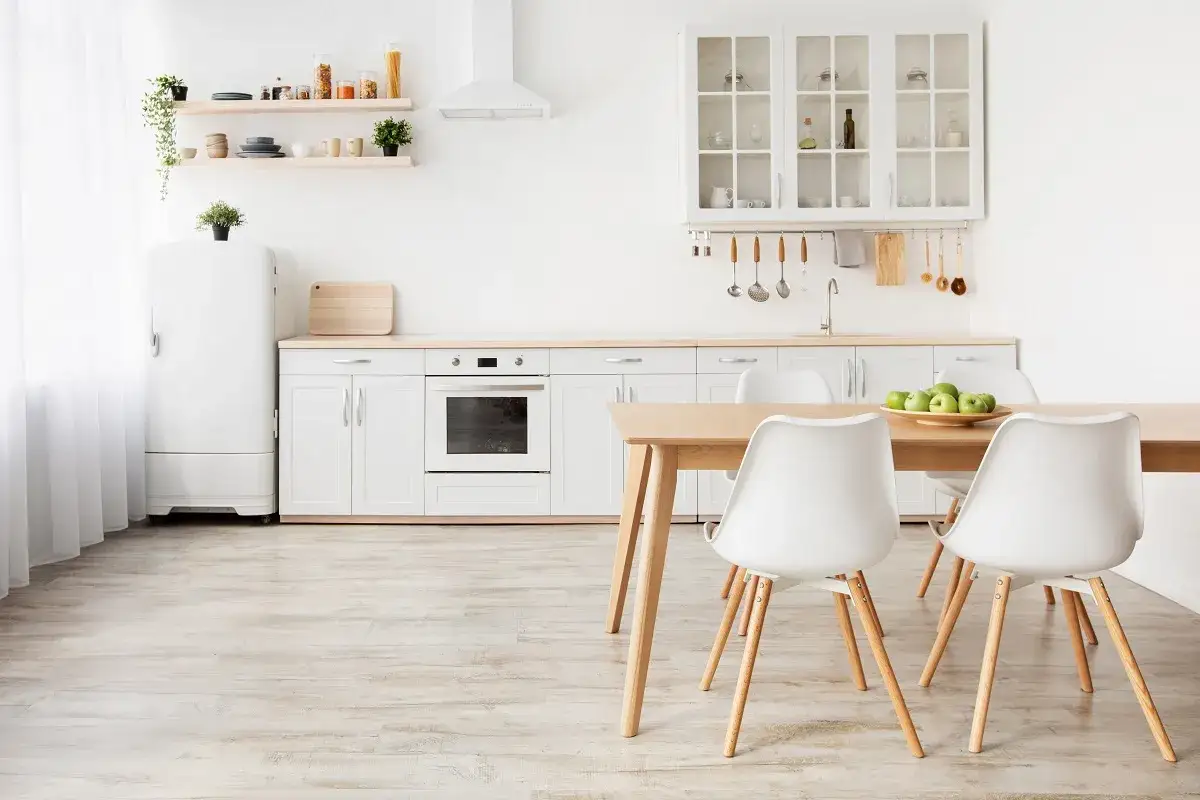 Cocina luminosa y moderna, ideal para decorar piso antiguo alquiler. Muebles blancos, electrodom&eacute;sticos integrados y mesa de madera con sillas.