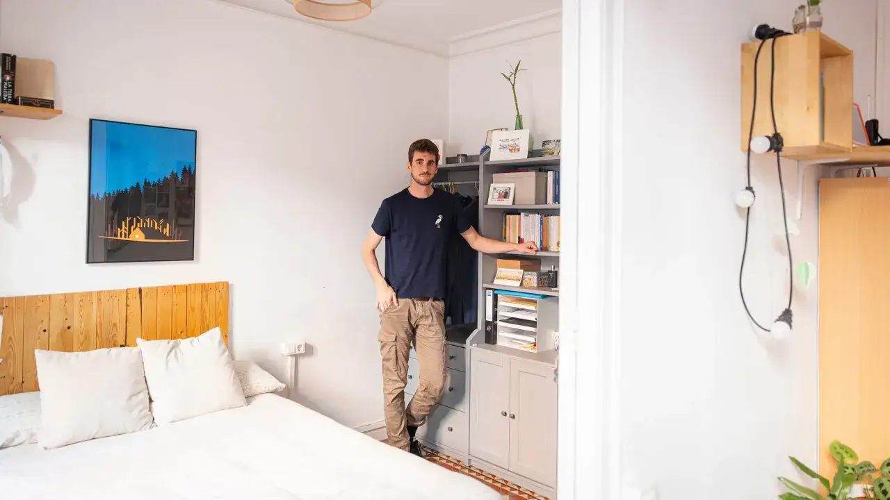 Joven en habitaci&oacute;n con cama y estanter&iacute;a. En Barcelona, es legal alquilar habitaciones, y este espacio parece listo para un inquilino.
