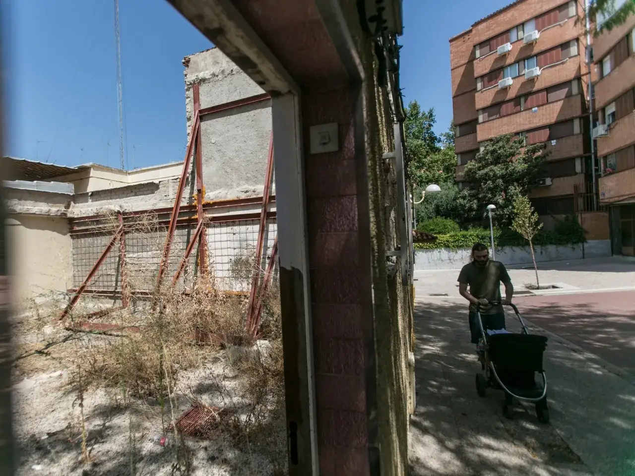 Hombre pasea carrito bebé junto a casa en ruinas. El ayuntamiento debe atender estas obligaciones.