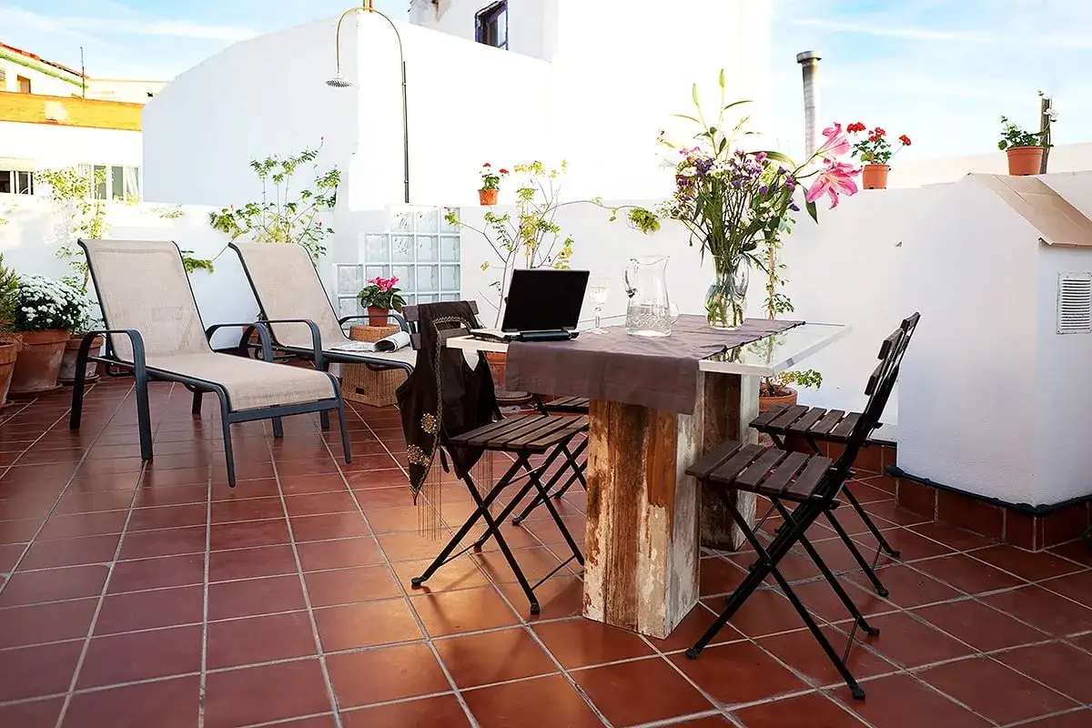 Terraza con tumbonas, mesa y sillas, ideal para uso privativo. Flores y plantas decoran el espacio.