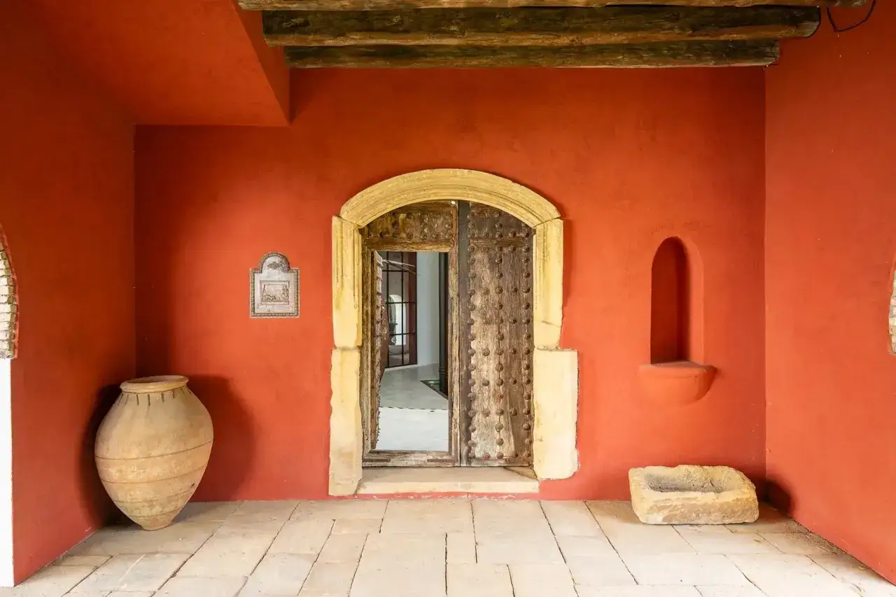 Entrada a casas curiosas con gran jarr&oacute;n de barro y puerta de madera antigua.