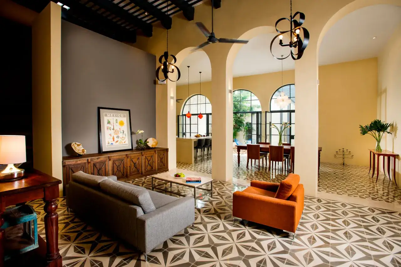 Sof&aacute; gris y sill&oacute;n naranja en un sal&oacute;n con suelo de baldosas geom&eacute;tricas. Las paredes en tonos tierra y ocre crean c&aacute;lidos colores para salones.