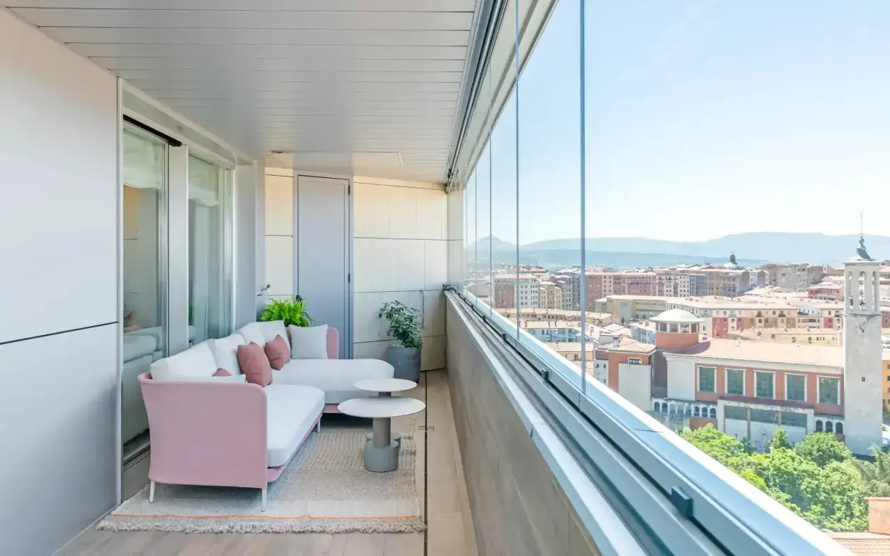 Acogedor sal&oacute;n en terrazas cerradas peque&ntilde;as con vistas a la ciudad. Sof&aacute; rosa y blanco, mesas auxiliares y plantas.