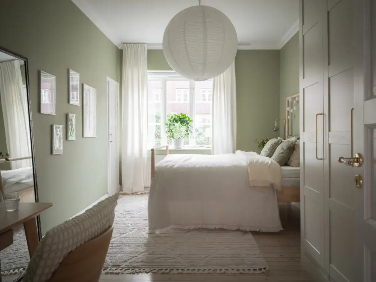 Habitaci&oacute;n serena con paredes verde pistacho, cama blanca y detalles en madera. Los colores que combinan con el verde pistacho resaltan la calma.