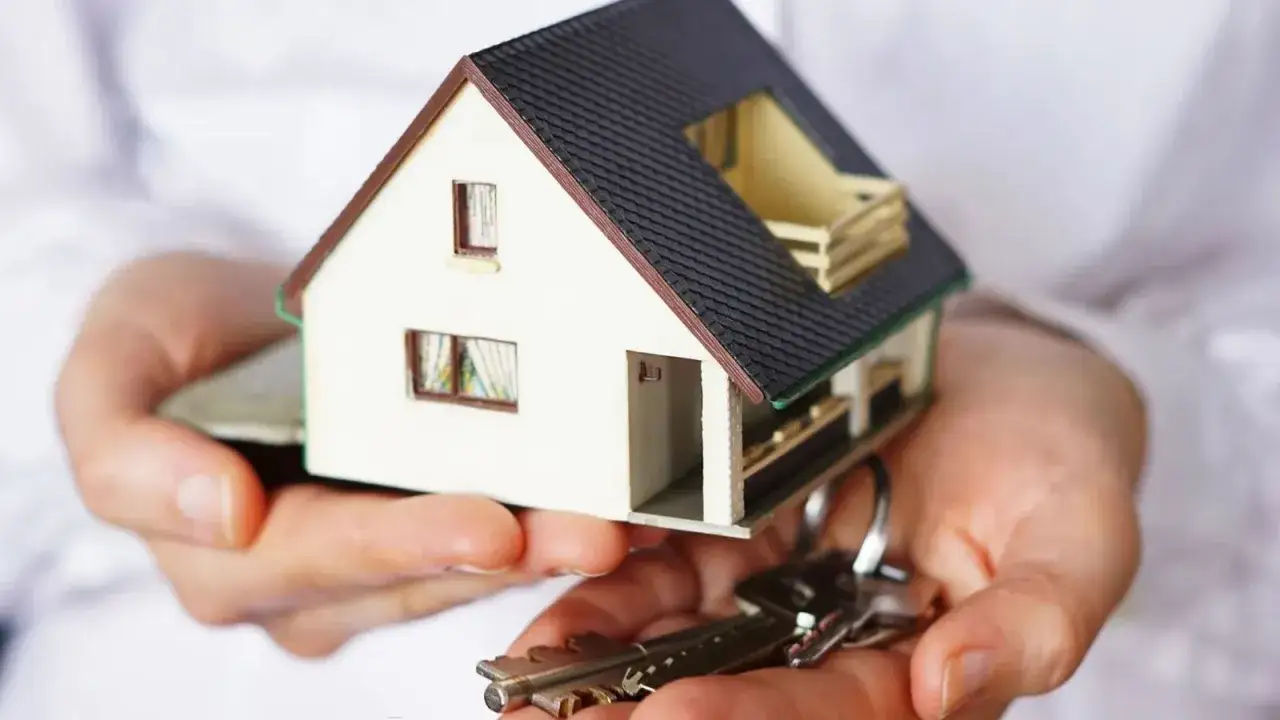 Manos sostienen una maqueta de casa y llaves, simbolizando el sue&ntilde;o de comprar vivienda a medias padre e hijo.