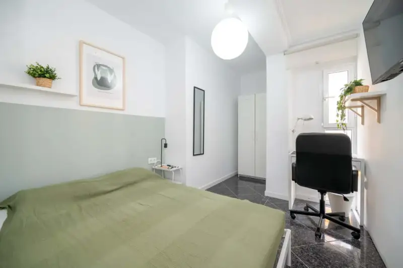 Habitación luminosa con cama, escritorio y armario. Ideal como piso para estudiantes, con decoración moderna y plantas.