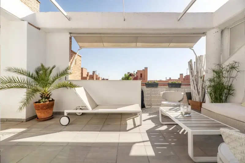 Encantadora decoracion terrazas aticos: tumbona, mesa de centro, sillón y plantas crean un oasis urbano.